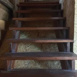 Drewniane schody w surowym wnętrzu z płyt OSB, widok z dołu, podkreślona struktura drewna i surowość wykończenia.