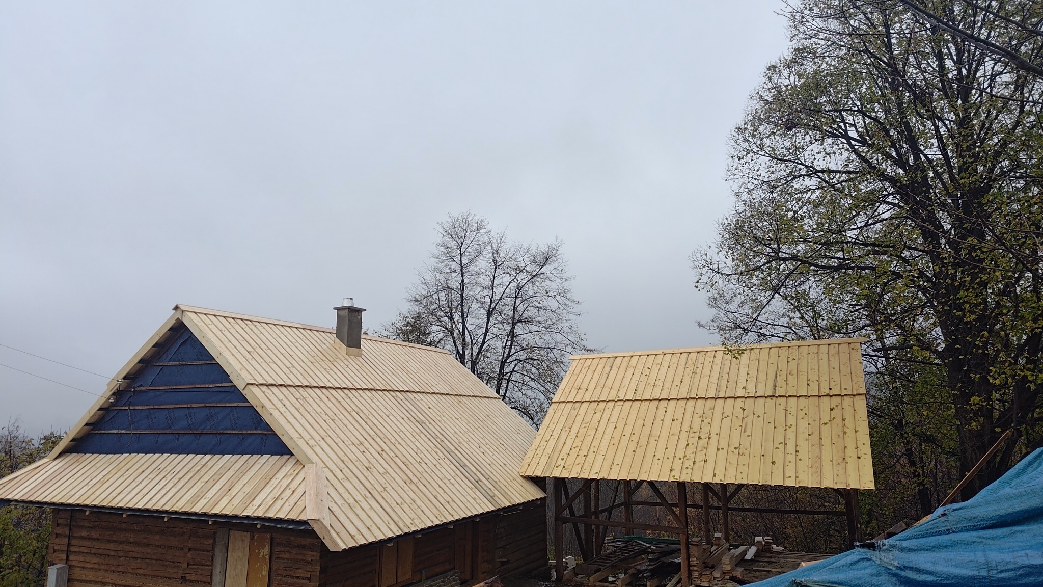 Dwa budynki w trakcie budowy dachu z drewnianych desek; jeden budynek ma już położoną membranę na części dachu, a drugi ma otwartą konstrukcję.