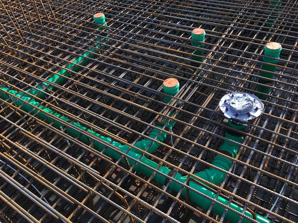 Zbrojenie fundamentu z zielonymi rurami instalacji podposadzkowej i zaślepkami na pionach kanalizacyjnych.