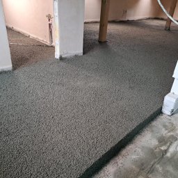 P&G POSADZKI - Wylana, świeża posadzka jastrychowa w pomieszczeniu z widocznymi elementami konstrukcyjnymi i instalacjami. Szara powierzchnia posadzki wypełnia całą przestrzeń.