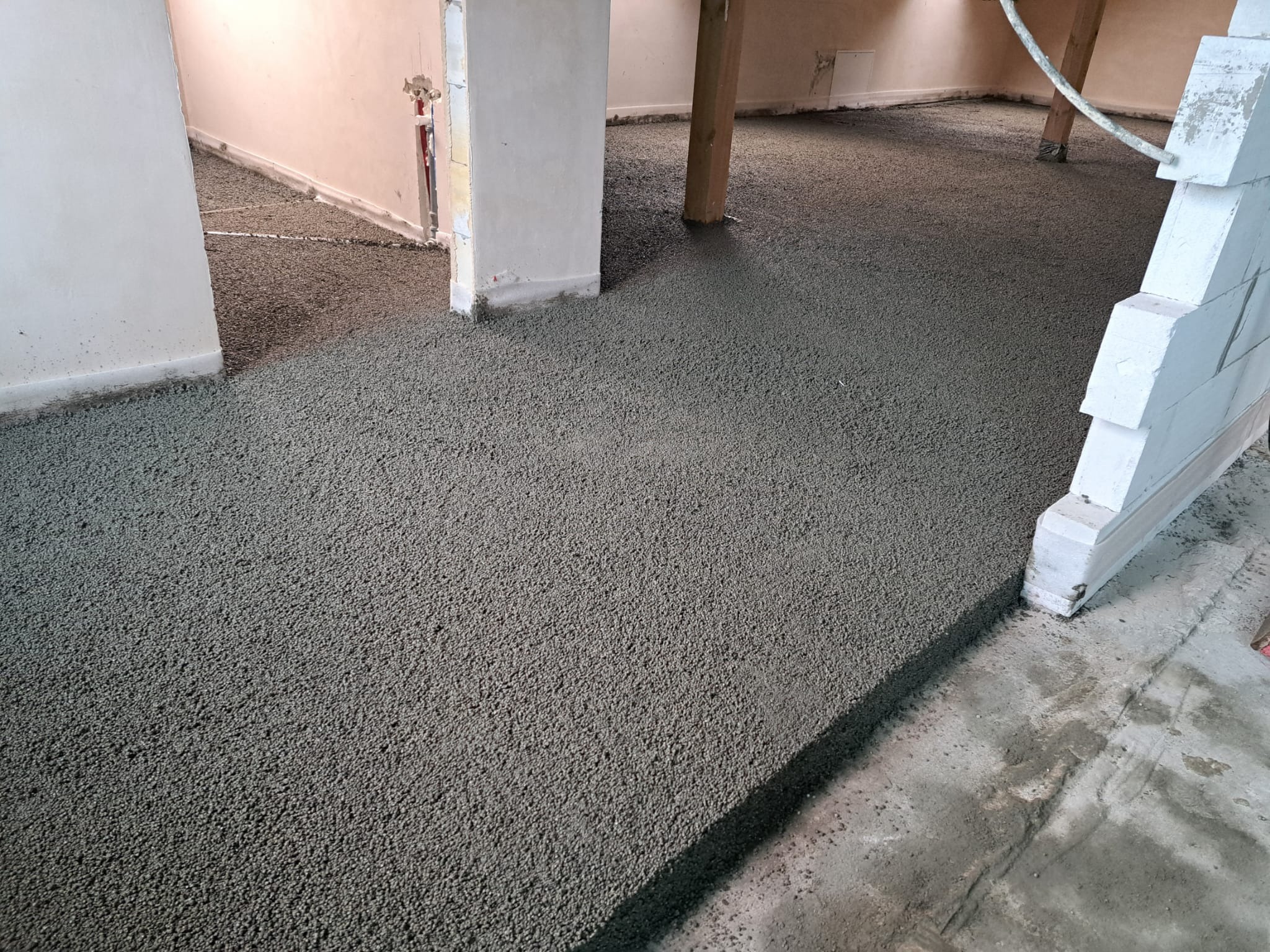 Wylana, świeża posadzka jastrychowa w pomieszczeniu z widocznymi elementami konstrukcyjnymi i instalacjami. Szara powierzchnia posadzki wypełnia całą przestrzeń.