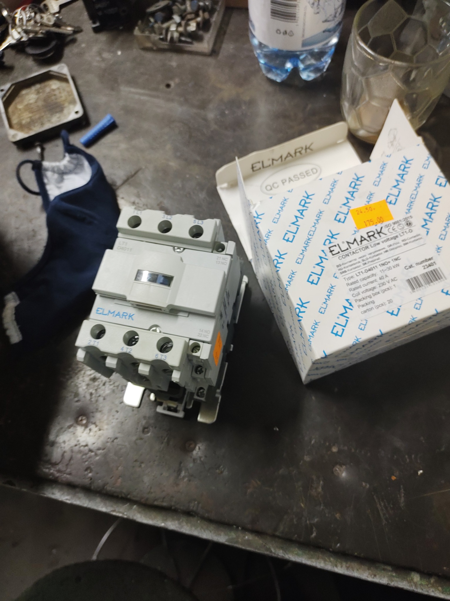 Stycznik ELMARK LT1-D4011 w oryginalnym opakowaniu na warsztatowym stole, obok butelki wody i szklanki. Na opakowaniu widoczna cena 175 zł.