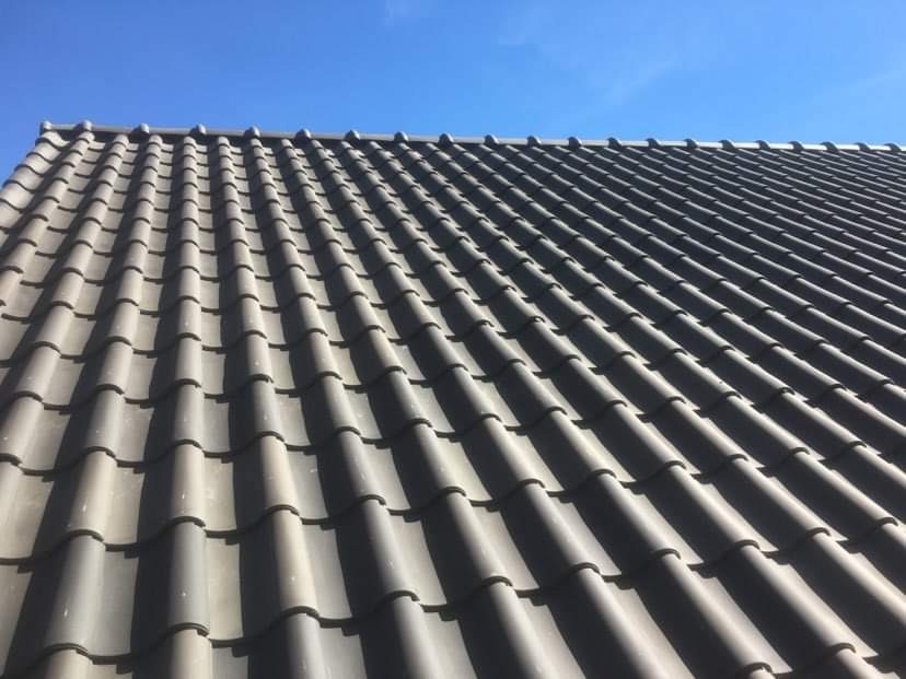 Nowy, grafitowy dach z dachówki ceramicznej ułożony w Skomlinie, widok z dołu na tle błękitnego nieba.