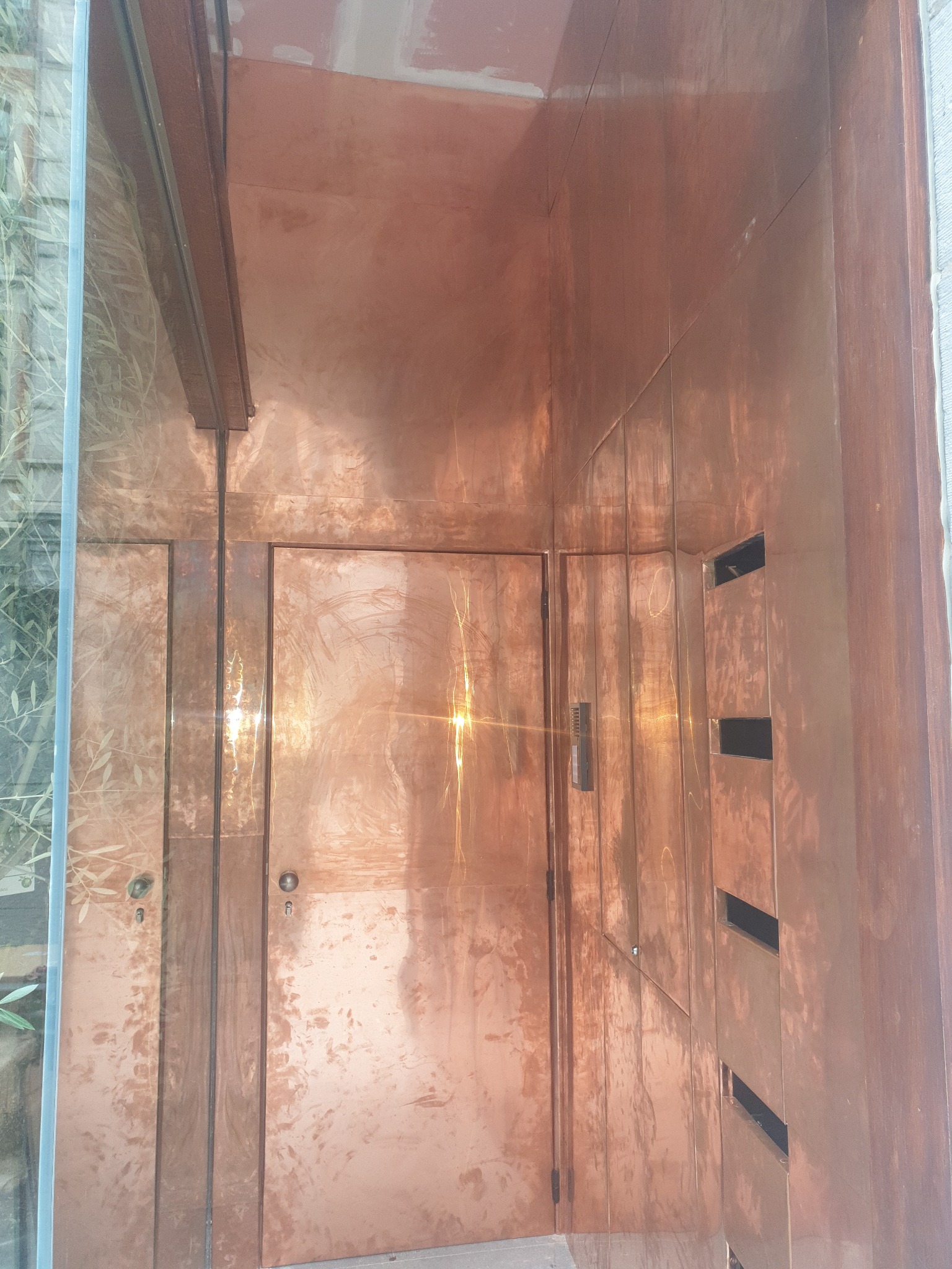 Miedziane wykończenie wnętrza z drzwiami i wnękami, widoczne refleksy świetlne i tekstura materiału.