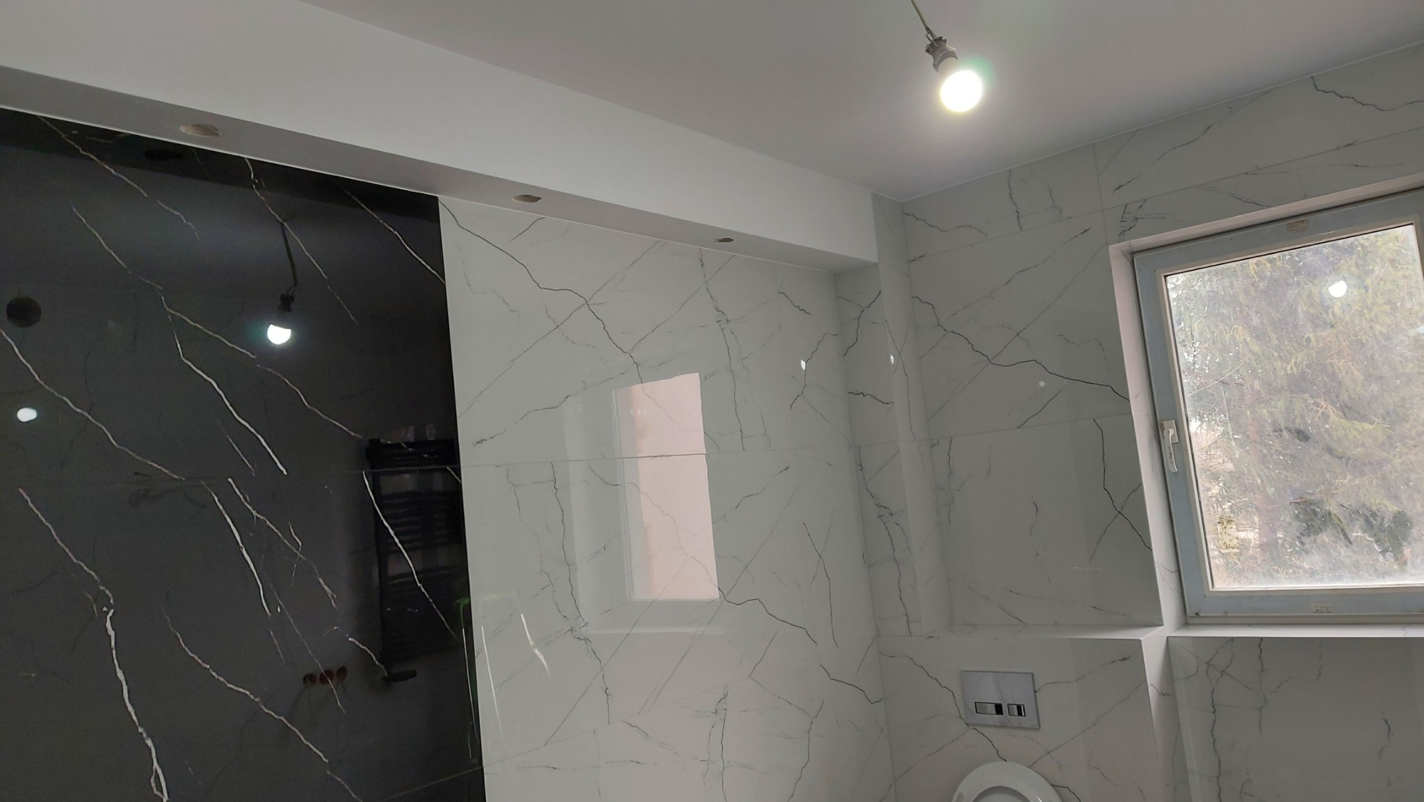 Wykończona łazienka w Białymstoku z czarno-białymi płytkami imitującymi marmur, widoczne okno i podwieszana toaleta.