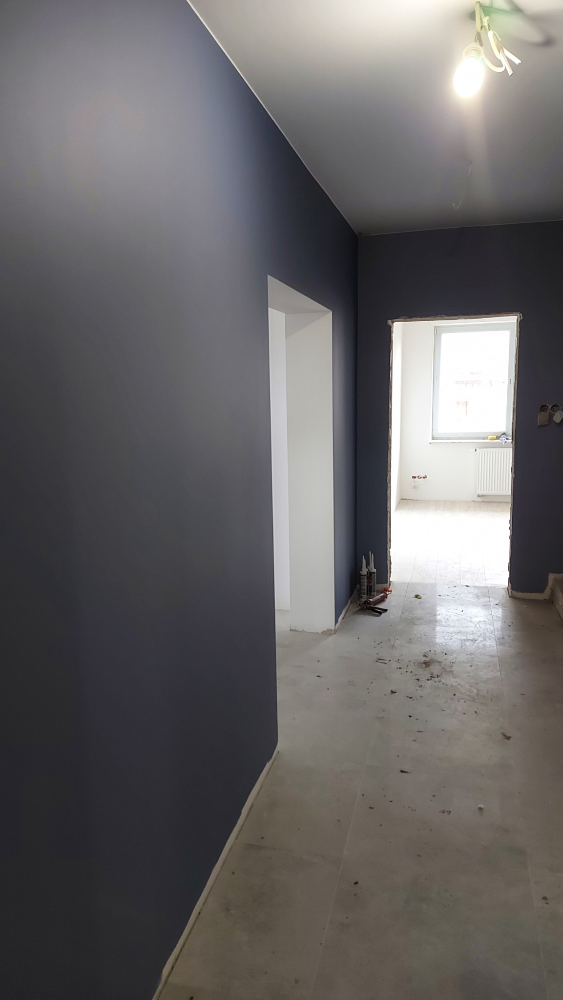 Świeżo pomalowane na ciemny kolor ściany w pomieszczeniu z widocznymi śladami po remoncie na podłodze i niedokończonymi obramowaniami drzwi.
