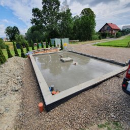 Gduli-Bud - Świeżo wylana płyta fundamentowa z wystającymi zbrojeniami, zabezpieczona folią kubełkową, widok z boku, zaparkowany samochód dostawczy w tle.