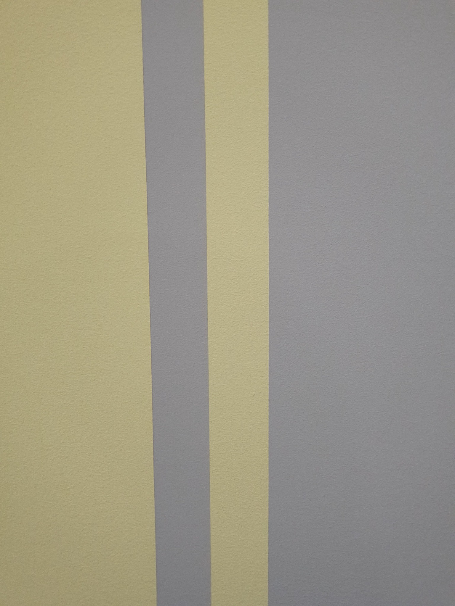 Fragment ściany pomalowanej w pionowe pasy w odcieniach szarości i jasnego beżu.