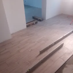 Ułożone panele podłogowe imitujące drewno, z widocznymi poziomicami i kartonami paneli w tle, częściowo zakryte folią.