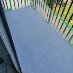 Balkon z nową, szarą, żywiczną posadzką, zabezpieczony folią i taśmą malarską przed zabrudzeniem balustrady.
