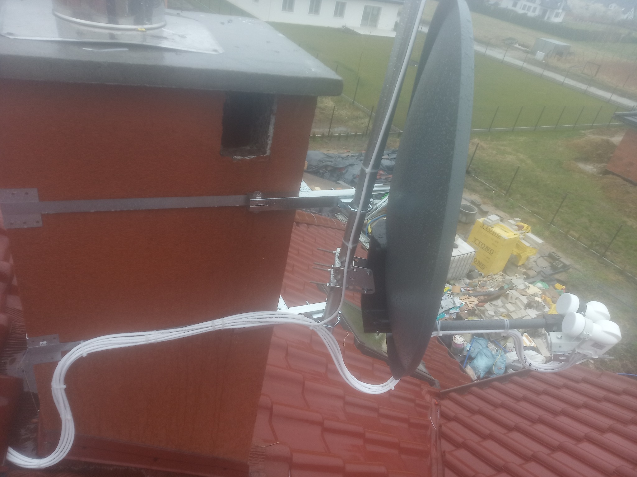 Antena satelitarna zamontowana na dachu obok komina, z widocznymi kablami i elementami mocującymi.