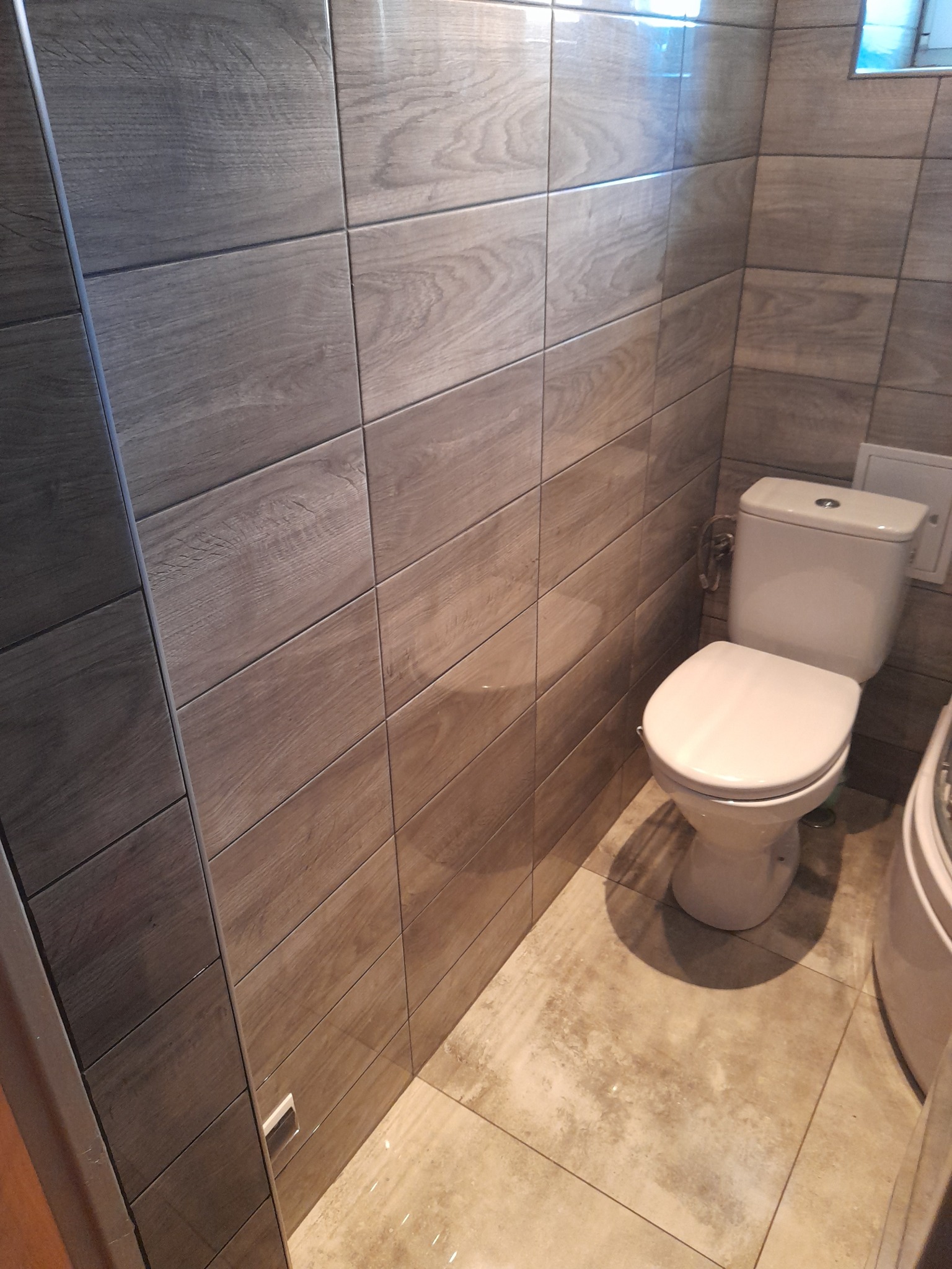 Toaleta w małej łazience z drewnopodobnymi płytkami na ścianach i podłodze.