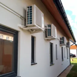 Zewnętrzne jednostki klimatyzacyjne zamontowane na elewacji budynku mieszkalnego, widoczne rury odprowadzające skropliny i przewody elektryczne.