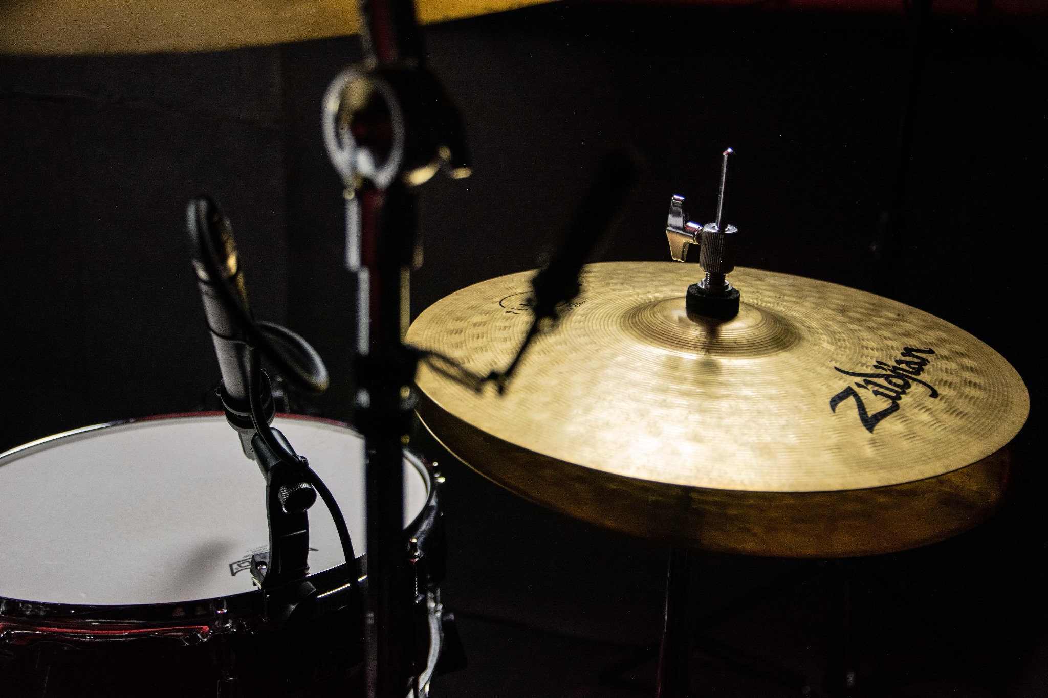 Złota blacha perkusyjna Zildjian z czarnym logo, mikrofon i fragment bębna w tle, oświetlenie studyjne.