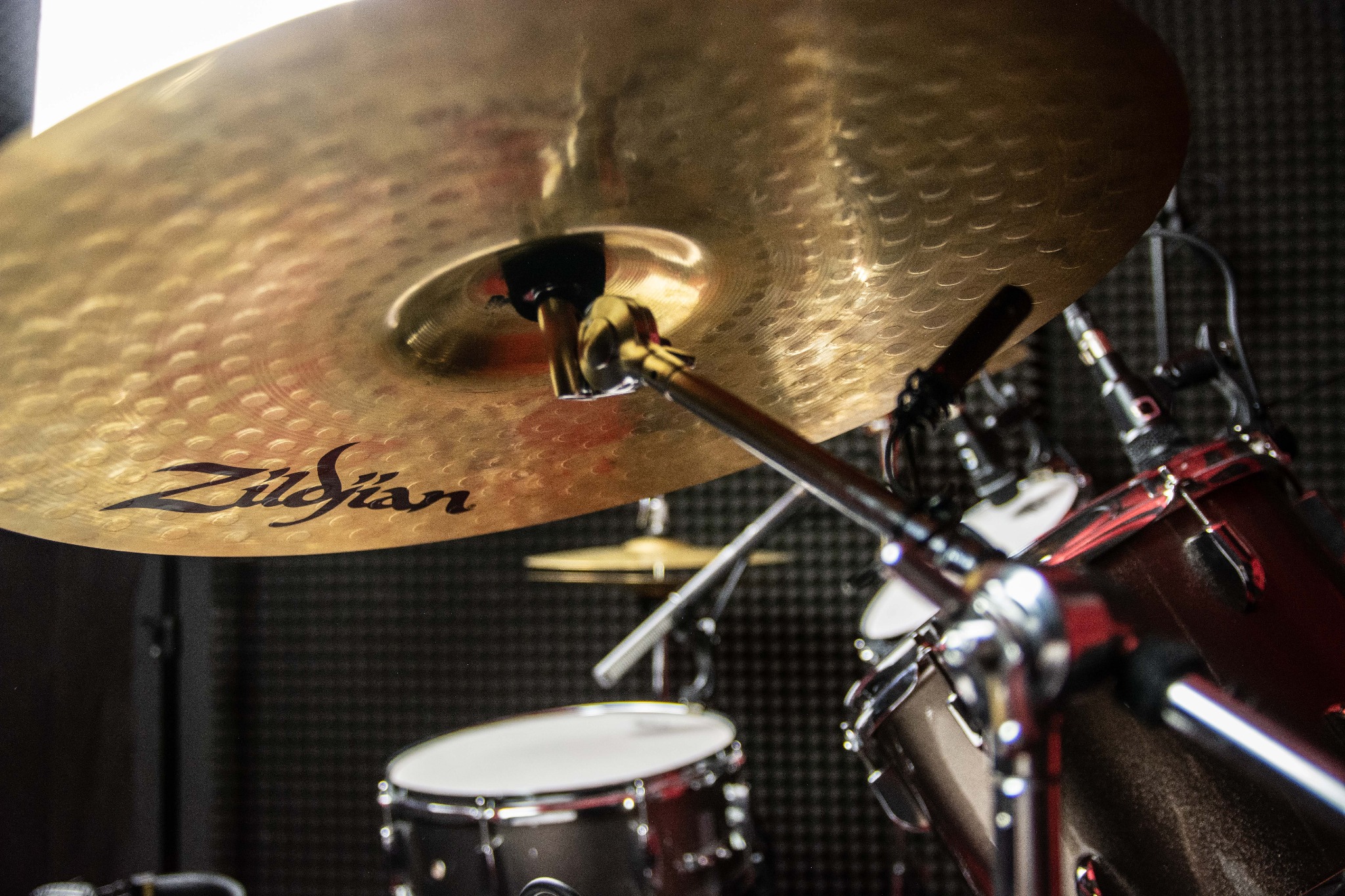 Złota blacha perkusyjna Zildjian z widocznymi śladami użytkowania i czarnym napisem, na tle akustycznej pianki i fragmentów zestawu perkusyjnego
