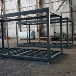 Szkielety konstrukcji stalowych w hali produkcyjnej w Zgorzelcu, przygotowane do budowy hali, widoczne wózki transportowe i zbiornik w tle.