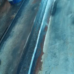 Spoina na grubej, pomalowanej na niebiesko konstrukcji stalowej, widoczne dwa wiadra farby przemysłowej w tle.