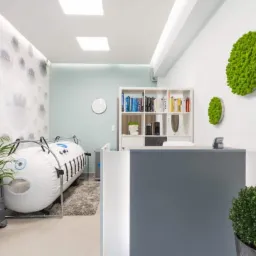 Wnętrze gabinetu z komorą hiperbaryczną, roślinami doniczkowymi i dekoracjami z mchu na ścianie.