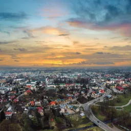 Panorama miasta z lotu ptaka o wschodzie słońca, widoczne budynki, drogi i rzeka.
