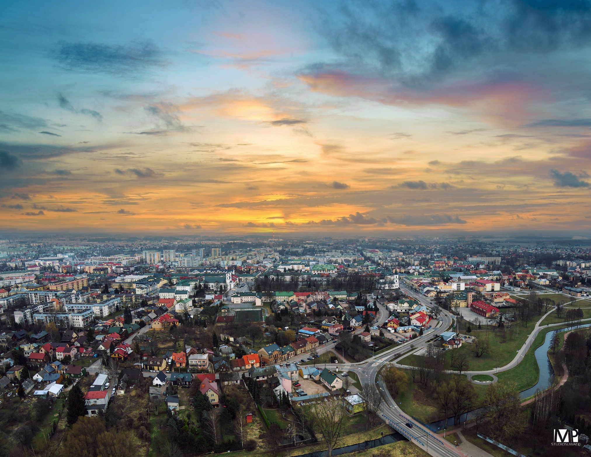Panorama miasta z lotu ptaka o wschodzie słońca, widoczne budynki, drogi i rzeka.