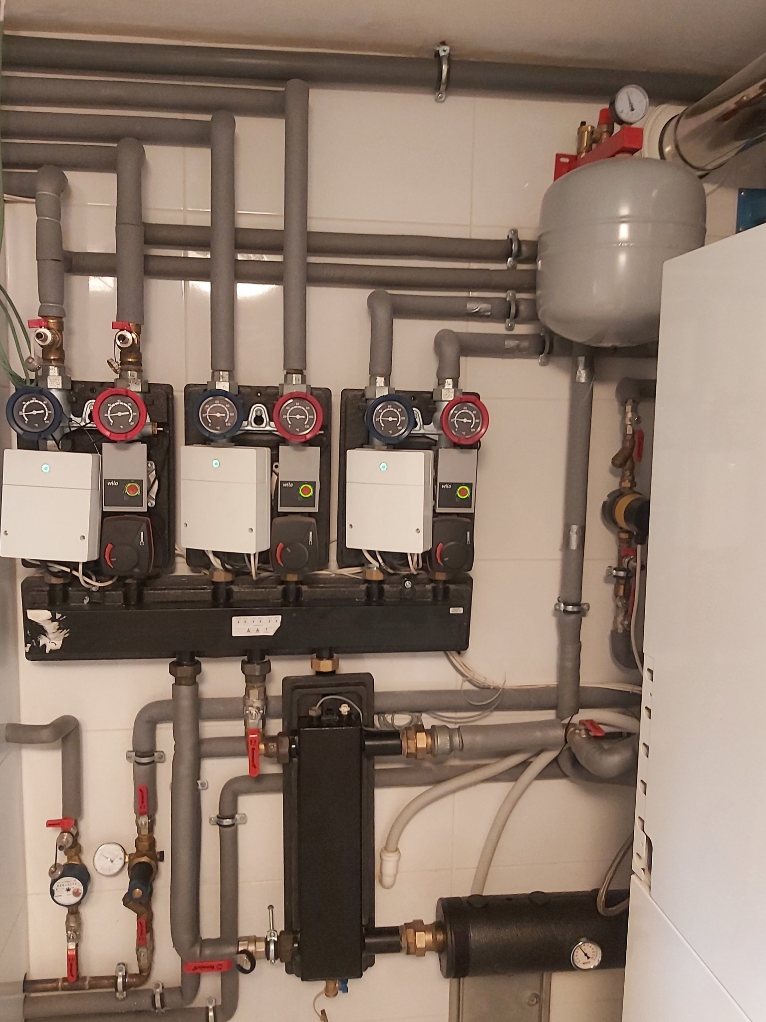 Rozdzielacz ogrzewania podłogowego z czterema obiegami, zasilany z kotła grzewczego, widoczne zawory, pompy obiegowe Wilo i rury w izolacji.