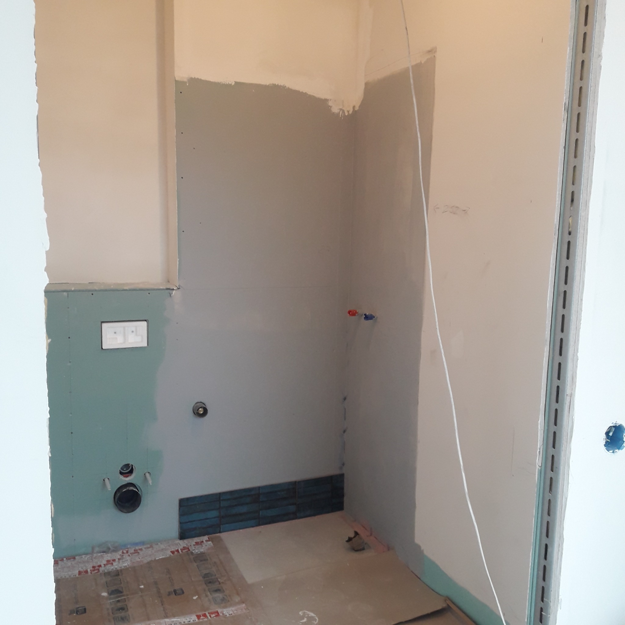 Niedokończony remont łazienki: widoczne surowe ściany z płyt gipsowo-kartonowych, częściowo pokryte szpachlą, przygotowane pod glazurę, z widocznymi otworami na instalacje i fragmentem ułożonych...