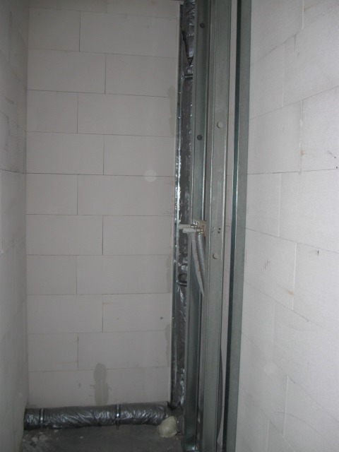 Ściana z białych bloczków, metalowy stelaż do zabudowy z płyt karton gips, widoczne przewody i rura wentylacyjna przy podłodze.