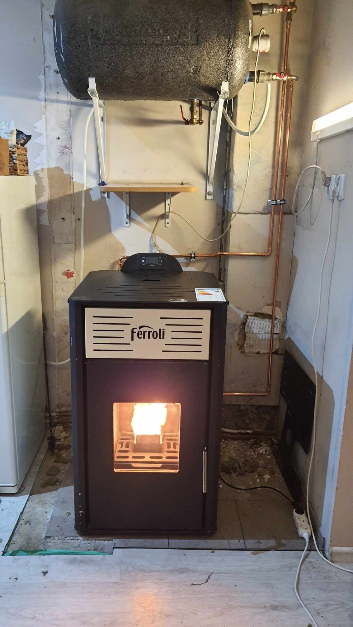 Zamontowany piec Ferroli na pellet z płomieniem w Olszynie, instalacja CO z miedzianych rur. Widoczny bojler na ścianie i fragment podłogi.