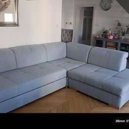 Tapicerstwo i Renowacja Andrzej Szopa - Szary narożnik z pikowanymi siedziskami w jasnym salonie z parkietem w jodełkę. W tle schody i komoda z dekoracjami.