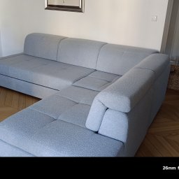 Tapicerstwo i Renowacja Andrzej Szopa - Jasnoszary narożnik z pikowanymi siedziskami w salonie z parkietem w jodełkę. W tle kominek i stolik z wikliny. Minimalistyczny design.