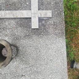 Czyściek - Płyta nagrobna z krzyżem z jasnego kamienia na tle trawy, z widocznym betonowym wazonem wypełnionym białymi kamykami i fragmentem butelki.