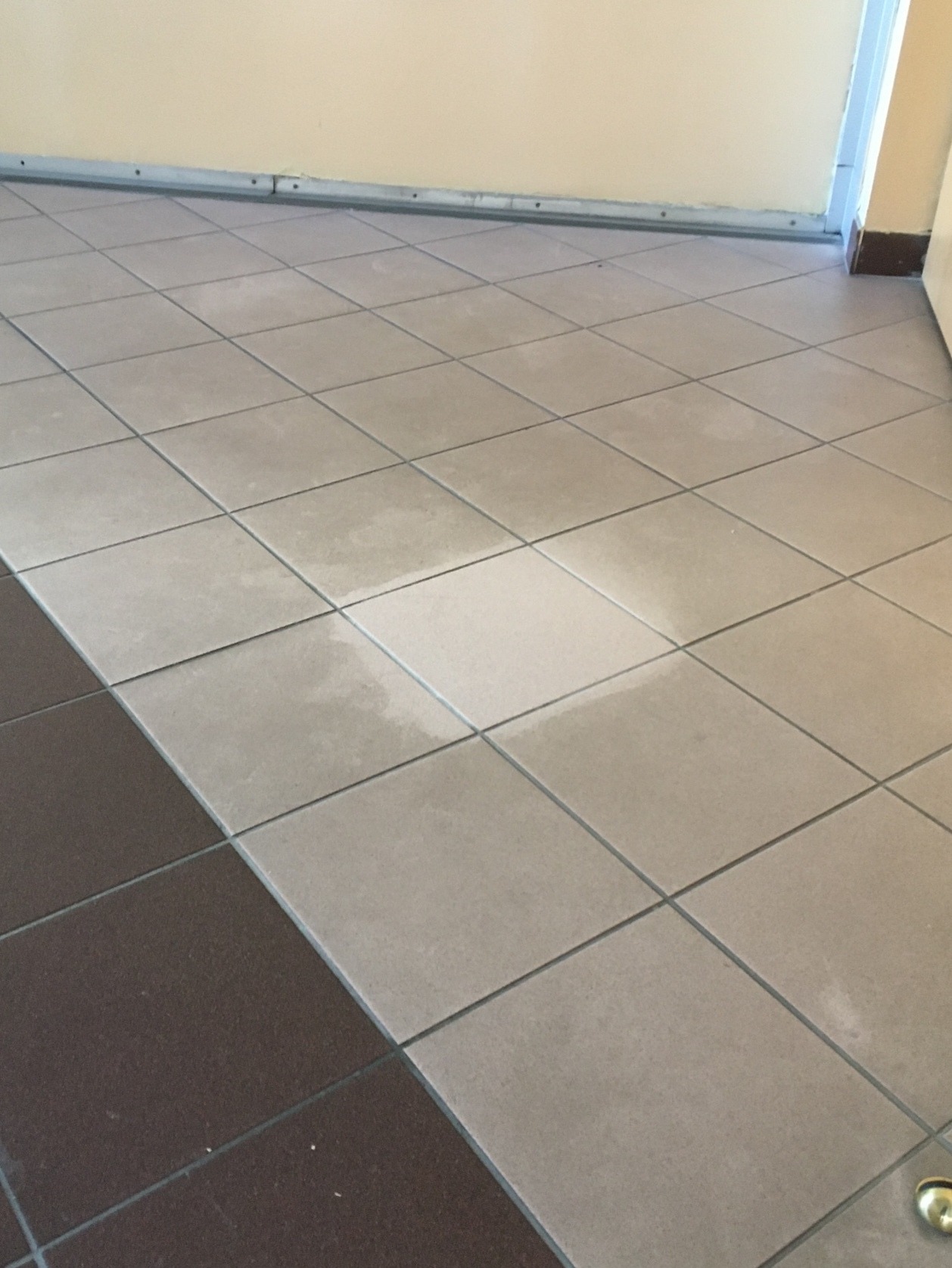 Umyta podłoga z płytek w dwóch odcieniach szarości, widoczna różnica w czystości między fragmentami podłogi.