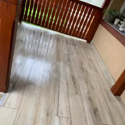 Balkon z drewnianą balustradą i nową podłogą z płytek imitujących drewno, widok z góry pod kątem.