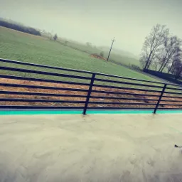 Czarna, pozioma balustrada z rurek na betonowym tarasie z widokiem na mglisty krajobraz; narzędzia i materiały budowlane leżą na podłodze.