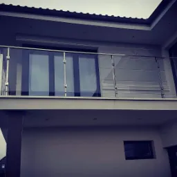 Nowoczesna balustrada ze stali nierdzewnej i szkła na balkonie domu w Kołobrzegu, widok z dołu na tle pochmurnego nieba.