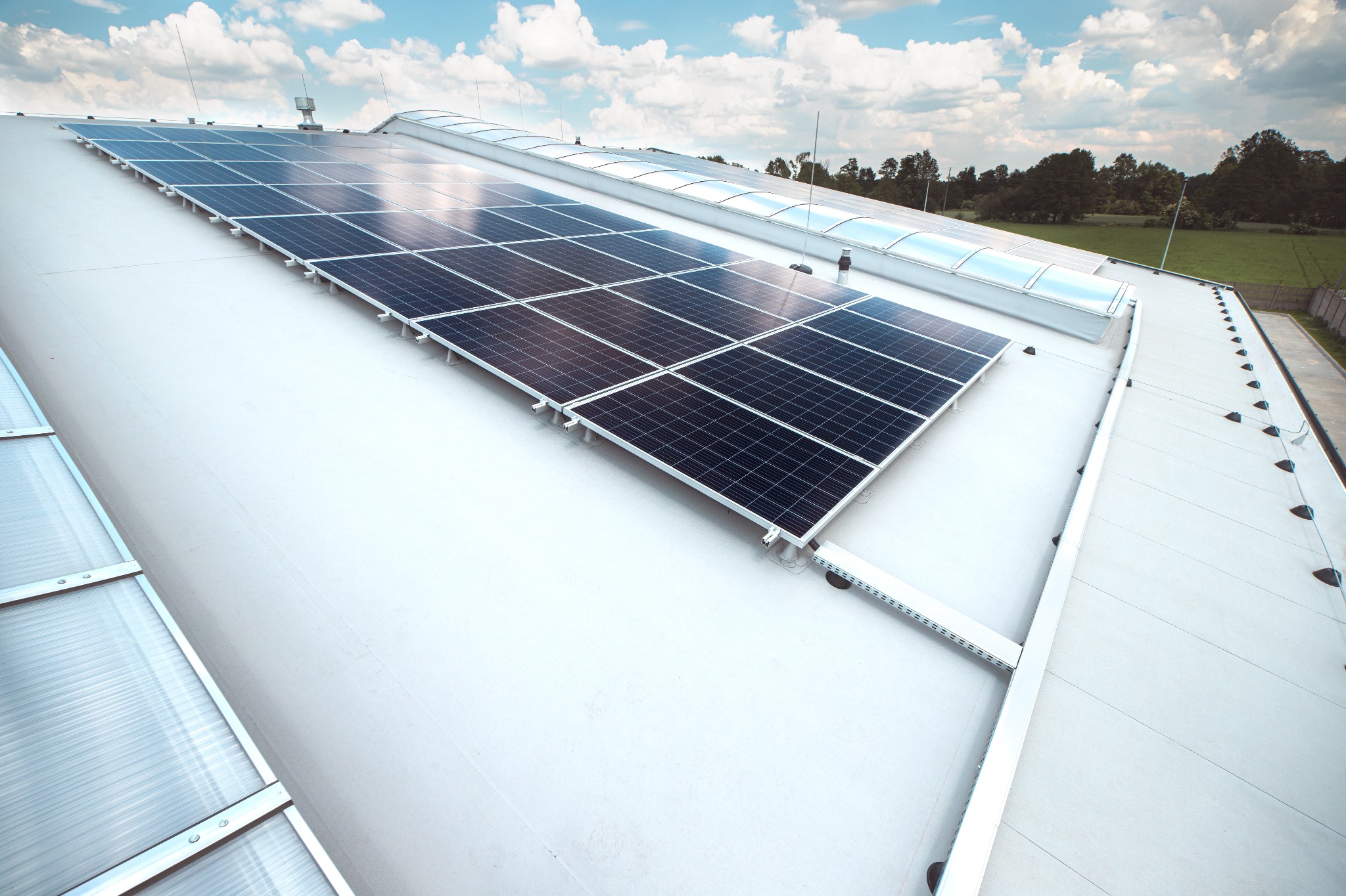 Instalacja paneli fotowoltaicznych na dachu hali przemysłowej z widocznymi świetlikami dachowymi i systemem odgromowym.