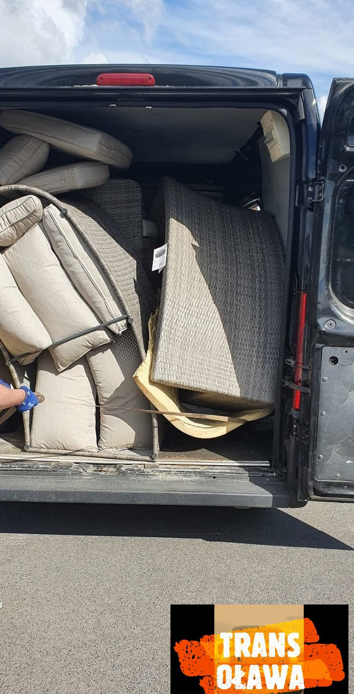 Wnętrze furgonetki załadowane rattanowymi meblami ogrodowymi i beżowymi poduszkami podczas transportu.