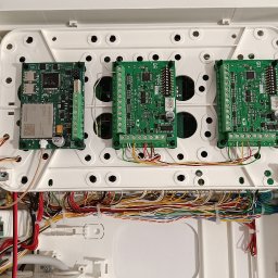 MIK-ELEKTRO Kamil Lipka - Otwarta skrzynka centrali alarmowej z widocznymi modułami elektronicznymi, licznymi przewodami w różnych kolorach i transformatorem na dole, zamontowana na białej ścianie.