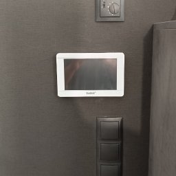 MIK-ELEKTRO Kamil Lipka - Panel sterowania Satel z ekranem dotykowym, włącznik światła i regulator temperatury zamontowane na szarej ścianie z teksturą.