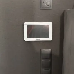 Panel sterowania Satel z ekranem dotykowym, włącznik światła i regulator temperatury zamontowane na szarej ścianie z teksturą.