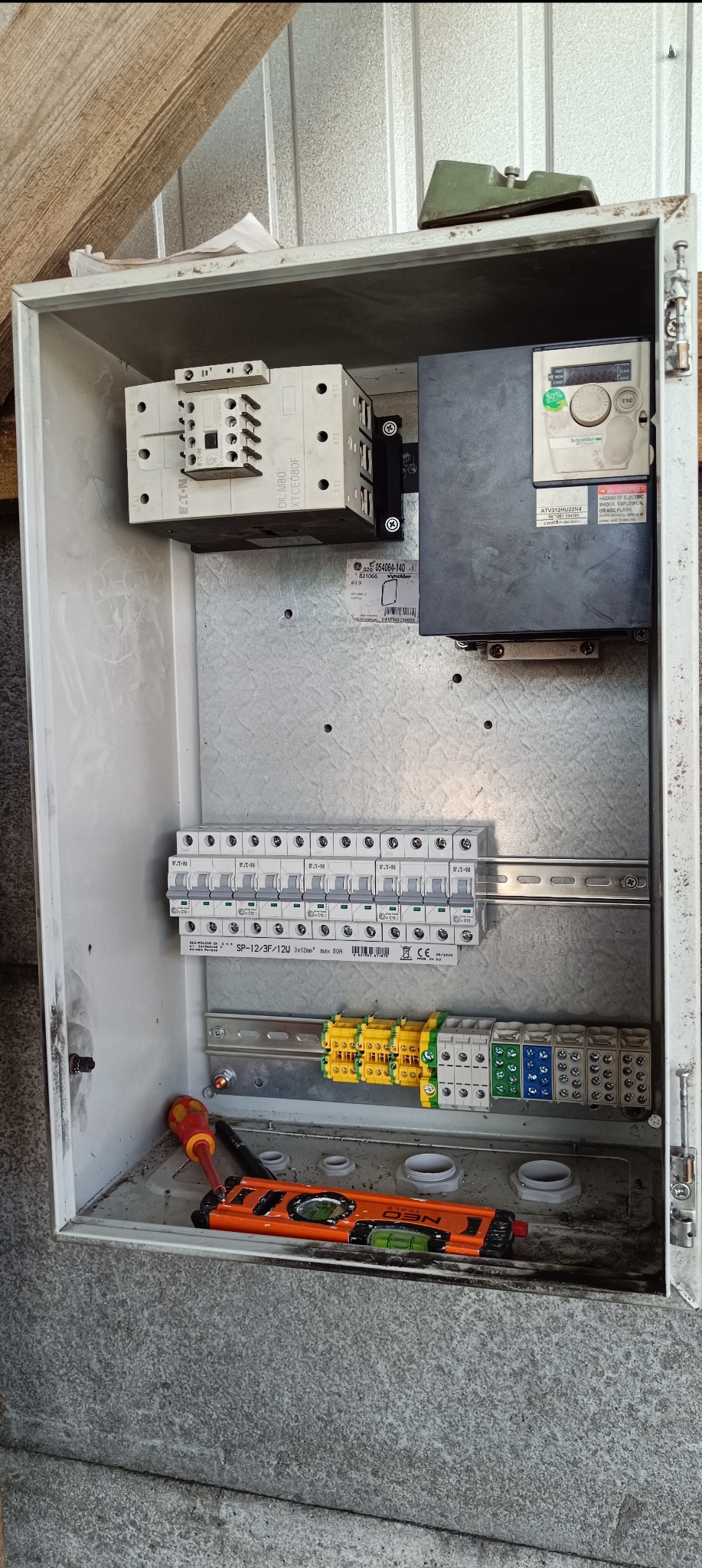 Otwarta skrzynka elektryczna z zamontowanymi elementami: stycznik EATON, falownik Schneider Electric, listwa z bezpiecznikami, złączki Wago, poziomica NEO i śrubokręt. Widoczne okablowanie...