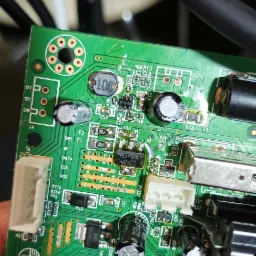 Zielona płyta główna urządzenia elektronicznego z widocznymi elementami SMD, kondensatorami i układami scalonymi, z bliska, prawdopodobnie uszkodzona.