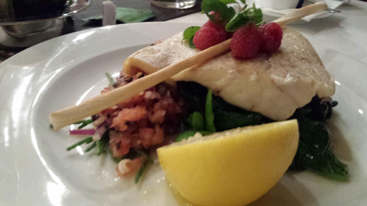 Elegancko podane danie z ryby z malinami, cytryną i zielonymi warzywami na białym talerzu. Dekoracja z grissini. Bliski kadr.