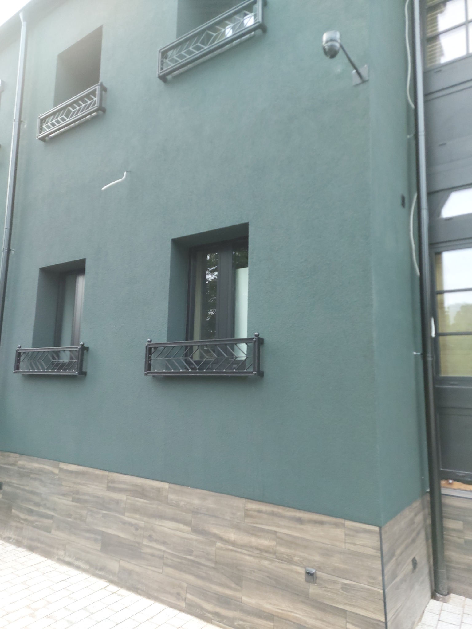 Elewacja budynku z zielonym tynkiem strukturalnym, dekoracyjnymi balustradami okiennymi i okładziną imitującą drewno na dole ściany.