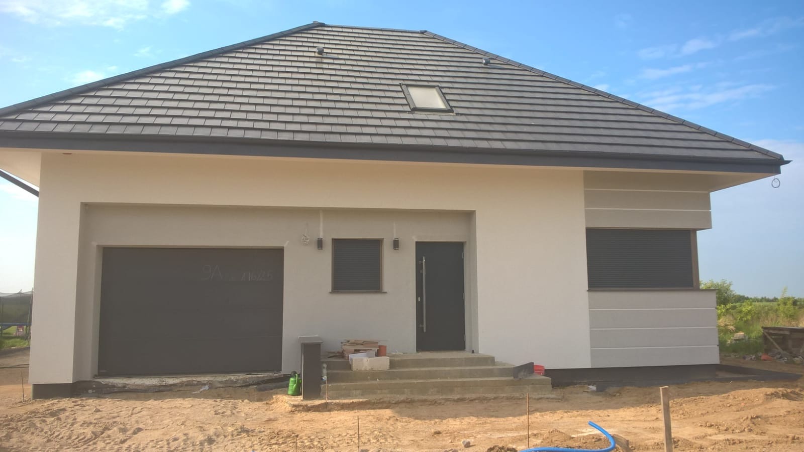 Nowoczesny dom jednorodzinny z szarą dachówką i jasną elewacją, widoczne prace wykończeniowe wokół budynku, Gryfino.