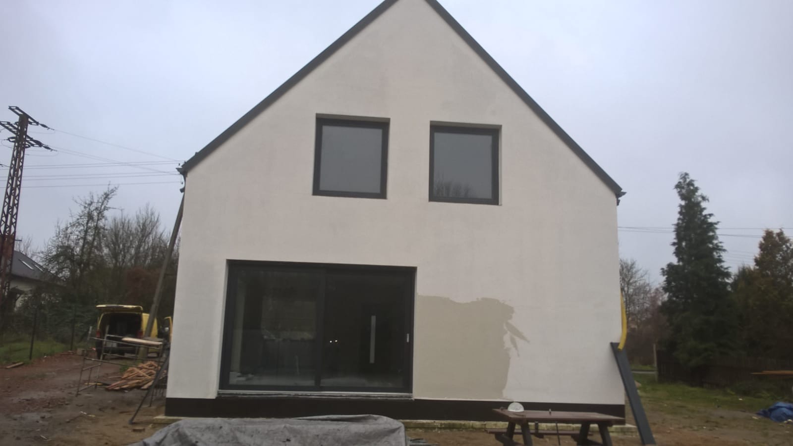 Dom jednorodzinny w trakcie tynkowania elewacji, fragment ściany z surowym tynkiem, widoczne okna i drzwi przesuwne.