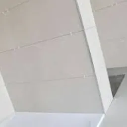 Białe, błyszczące płytki na ścianie i podłodze, ułożone w regularny wzór. Widoczna fuga i fragment narożnika. Minimalistyczne wykończenie wnętrza.