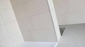 Białe, błyszczące płytki na ścianie i podłodze, ułożone w regularny wzór. Widoczna fuga i fragment narożnika. Minimalistyczne wykończenie wnętrza.