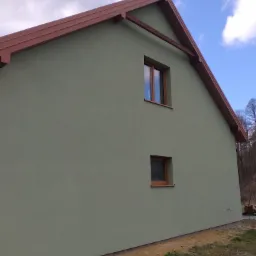 Ocieplony dom w kolorze oliwkowym z brązowymi oknami i dachem, widok z boku na tle błękitnego nieba z chmurami.