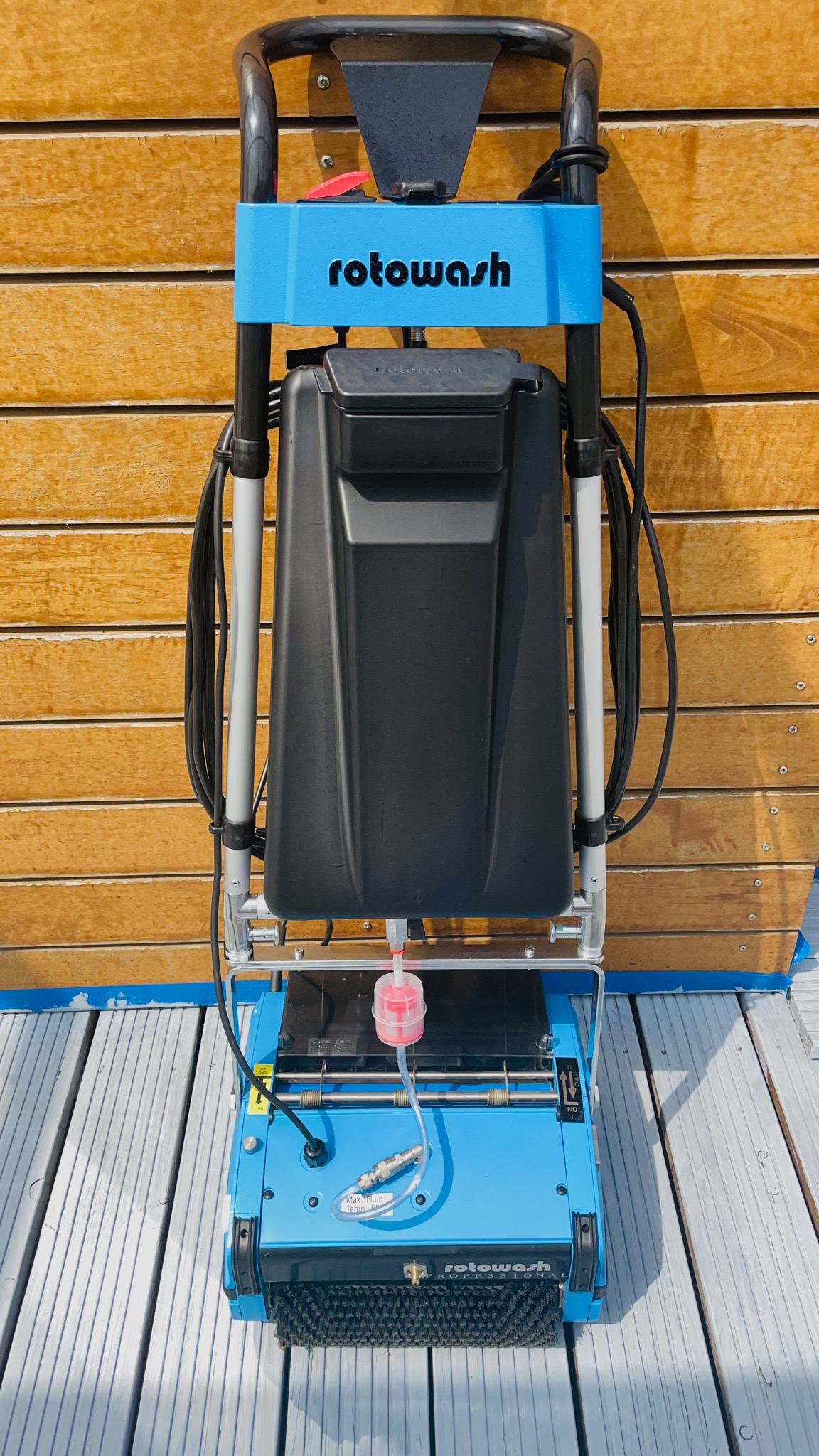Niebieska maszyna Rotowash do czyszczenia powierzchni, widok z przodu, na tle drewnianej ściany i szarego podłoża.